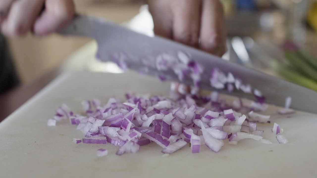 Close up, a chef chopping red onion with a chef's knife on a white cutting board