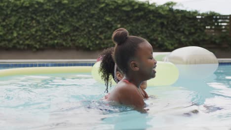 happy african american mother and daughter playing in swimming pool in garden, slow motion