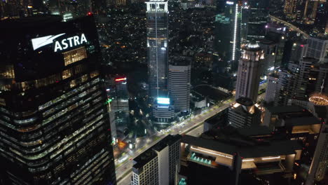 Close-up-fly-by-aerial-shot-of-modern-tall-skyscrapers-at-night-with-busy-car-traffic-below-in-Jakarta