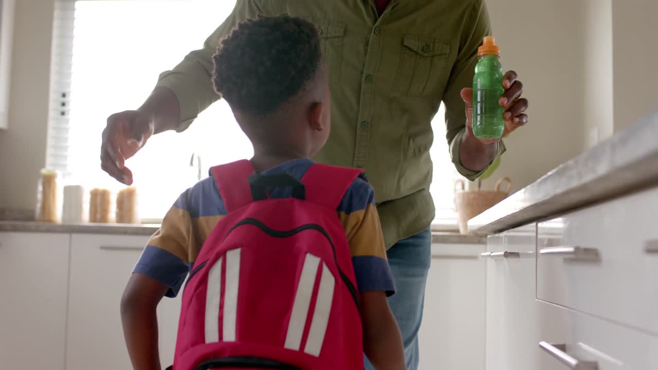 Happy african american grandfather embracing with grandson in kitchen before school, slow motion