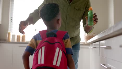 feliz abuelo afroamericano abrazando con su nieto en la cocina antes de la escuela, cámara lenta