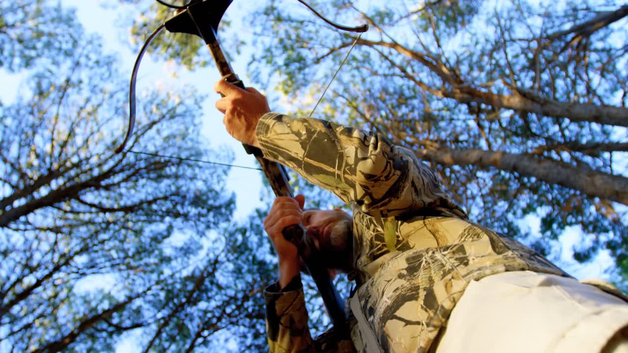 Homme visant avec un arc à poulies dans la forêt 4k