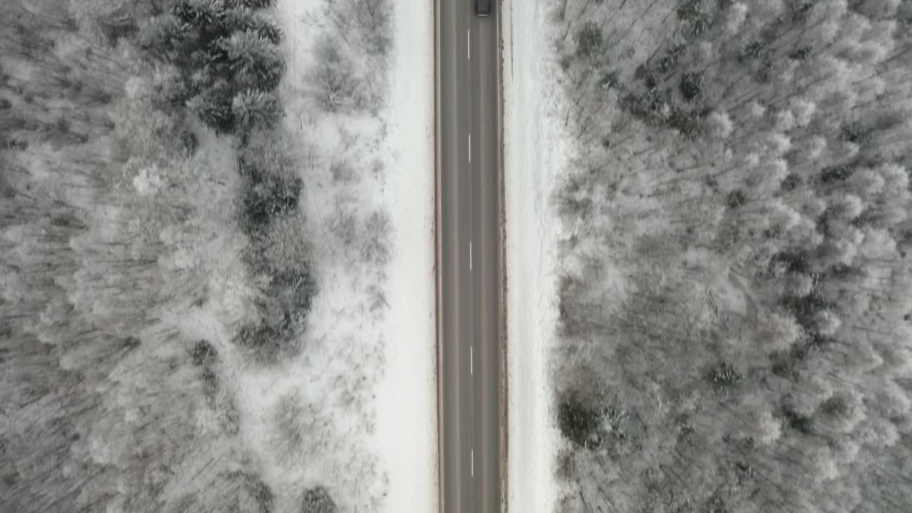 Car driving on a rural highway surrounded by snow covered trees. Aerial top down drone view of countryside road.