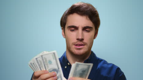 Man-counting-money-on-blue-background.-Satisfied-guy-holding-cash-in-studio