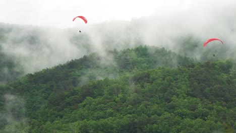 Zwei-Gleitschirme,-Die-Langsam-über-Den-Berg-Absteigen,-Der-Nach-Dem-Regen-Verdampft