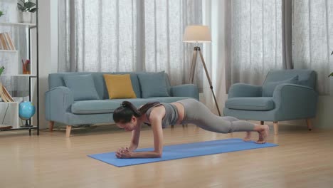 joven mujer atlética asiática con ropa deportiva haciendo yoga en el antebrazo en la postura de tabla en la alfombra en casa