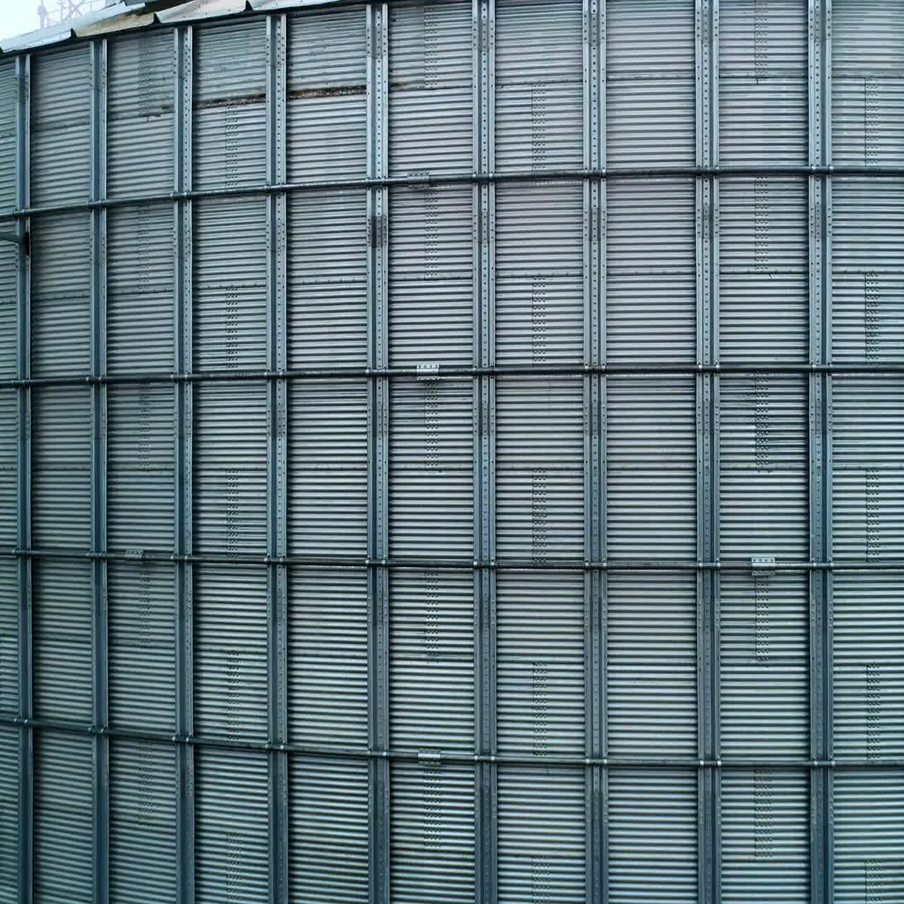 Metal surface of huge elevator container. Rising along the silver shell of granary tank up to the top. Foggy sky backdrop