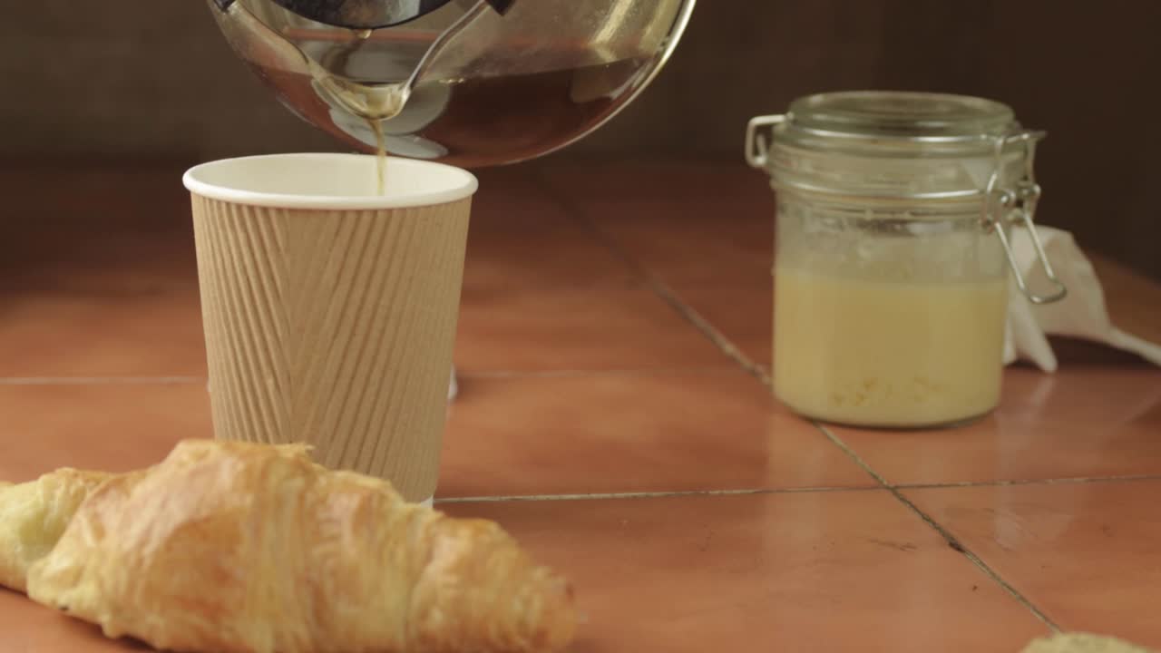 verter café recién hecho en una taza con pastelería de croissant de tiro medio.