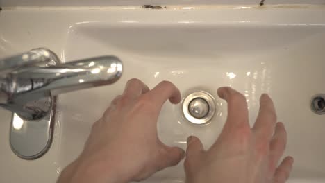 a pair of large hands letting the water drop off in the white sink