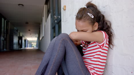 biracial girl appears upset, sitting alone with her head on her knees in school
