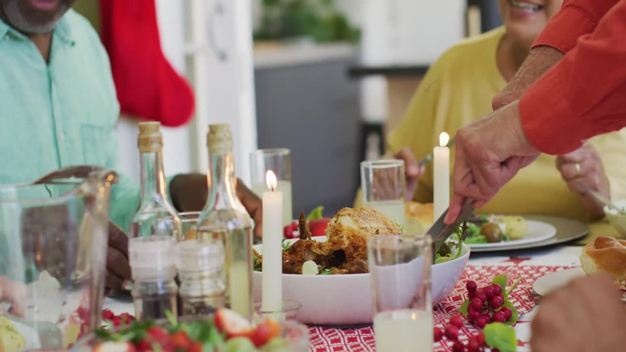 feliz hombre mayor afroamericano en santa hat hablando en la mesa de la cena de navidad con amigos