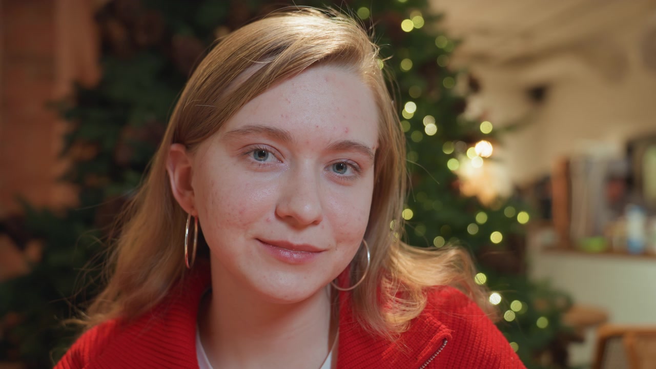 Young Woman Drinking from Mug and Smiling in Cozy Cafe with Christmas Tree