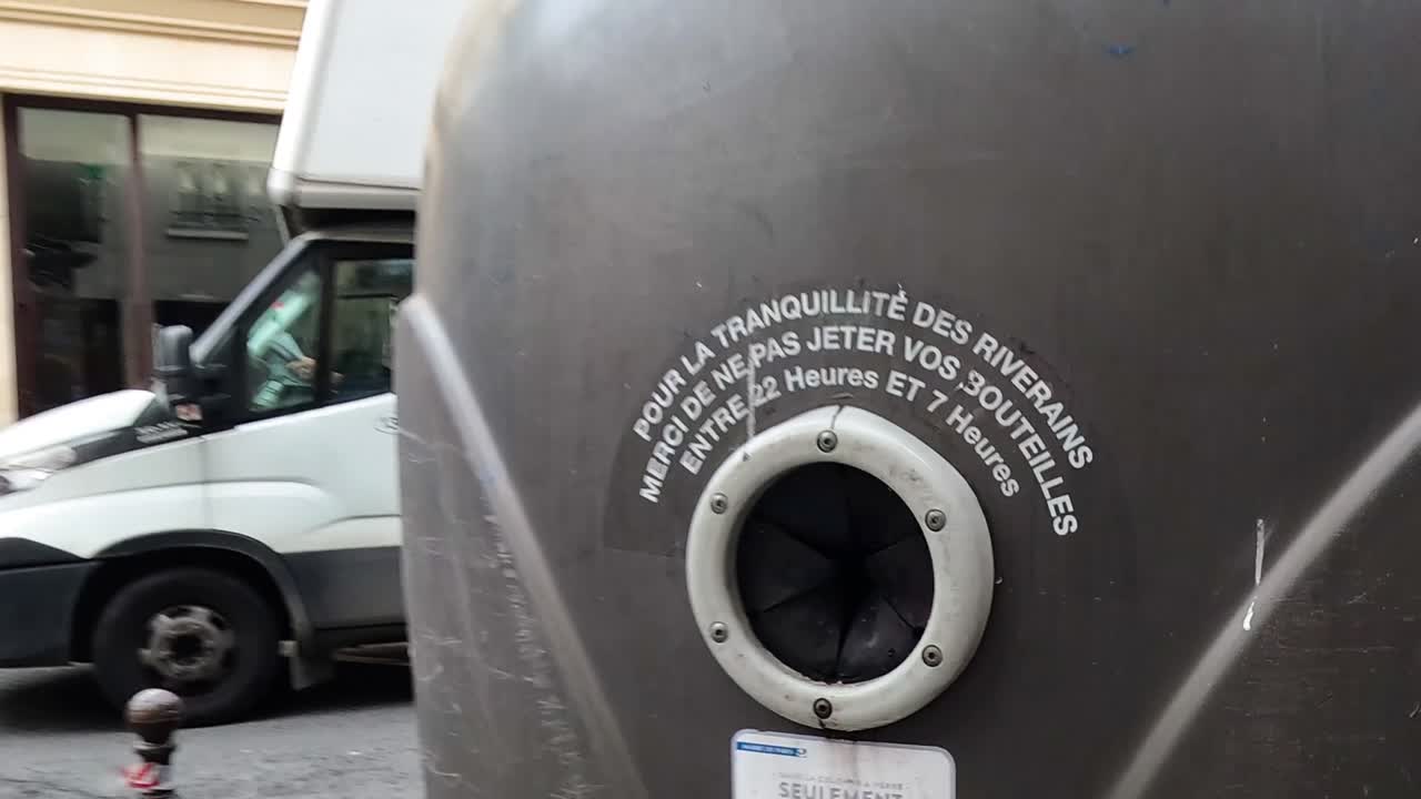 Detailed view of a recycling bin with passing vehicles on a city street.
