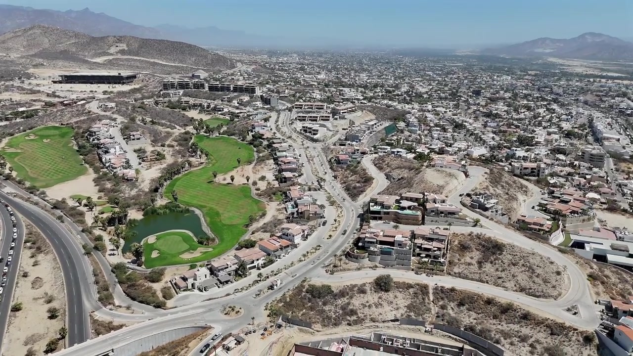 Drone panning right above a golf course in San José del Cabo, revealing the town, light traffic, and surrounding desert landscape on a sunny day.