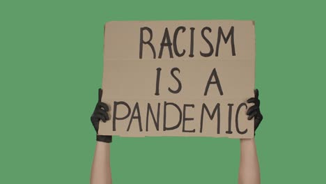 showing cardboard poster with inscription racism is a pandemic. human rights demonstration. hands holding a poster a green screen, chroma key. close up. slow motion