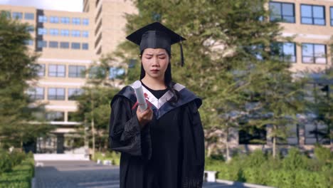 asian woman student in cap and gown looking at diploma then shaking her head being unsatisfied graduates in front of a magnificent university building