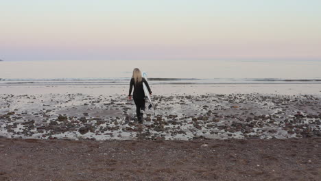 rear view of woman wearing wetsuit carrying surfboard walking into  sea