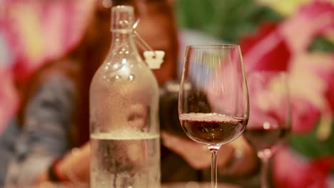 a person pours red wine into a glass, highlighting fine dining ambiance with soft lighting and floral background