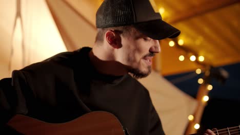 man plays the guitar and sings songs in a tent with light bulbs