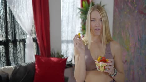 Hermosa-Rubia-Caucásica-Mujer-Blanca-Vestida-De-Fitness-Como-Influenciadora-De-Las-Redes-Sociales-Posando-Y-Comiendo-Pimientos-Naranjas-Y-Rojos-Promoviendo-Una-Alimentación-Saludable-Y-Un-Estilo-De-Vida-En-Youtube-Y-Tiktok