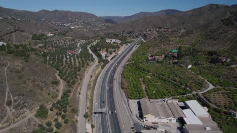 the road along which cars are driving is surrounded by rolling hills and lush greenery
