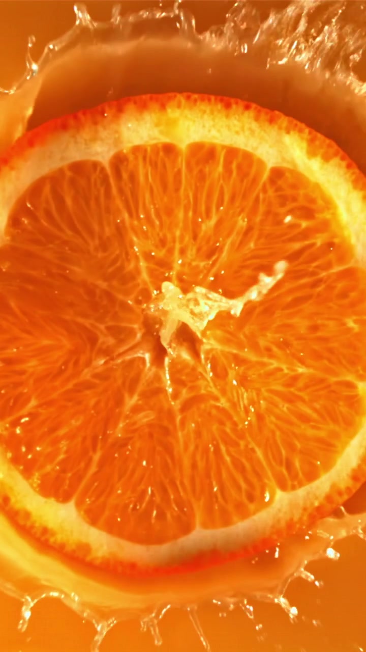 Fetta d'arancia vivace cade nel succo con schizzi al rallentatore