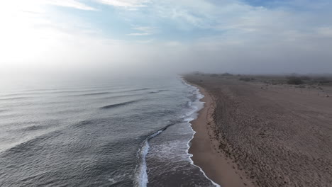 empty misty sunrise beach and shimmering rippled ocean coastline aerial view