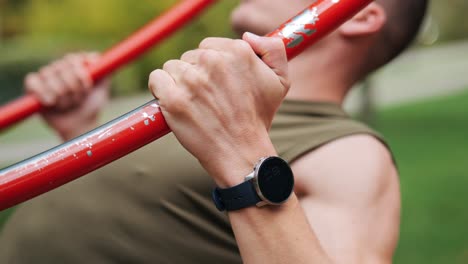 Fokussierter-Junger-Athletischer-Mann-Mit-Smartwatch,-Der-Klimmzüge-Auf-Der-Roten-Sportanlage-Im-Park-Macht