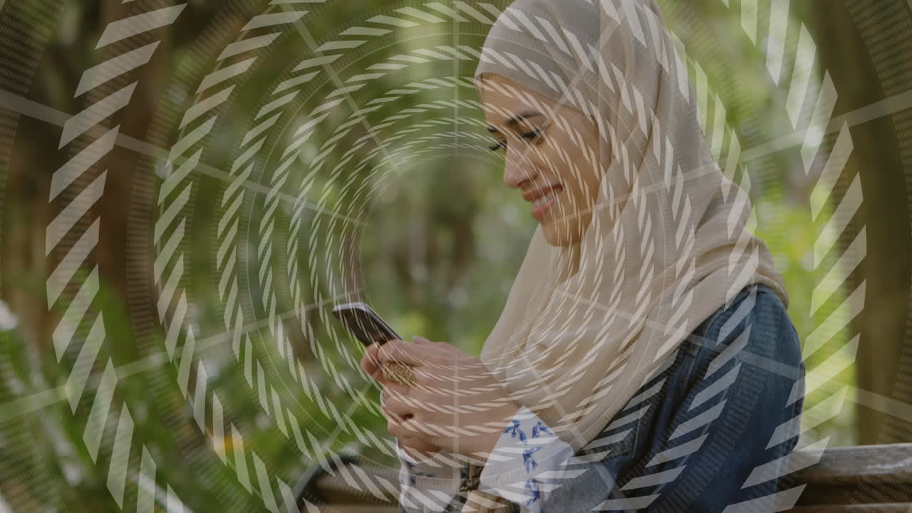 Woman wearing hijab using smartphone on bench in park, showing animated circular tech graphics
