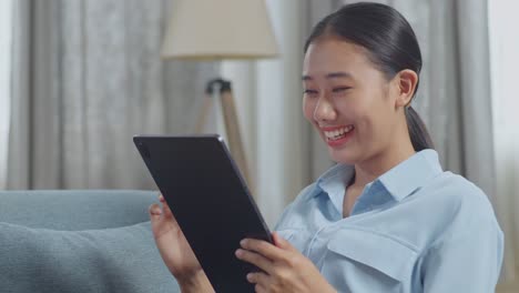 close up of asian woman enjoys using a tablet while lying on sofa in the living room