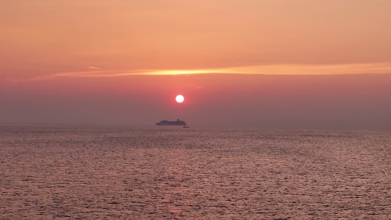 オレンジ色の夕焼け時の海に浮かぶ大型クルーズ船と小型漁船。