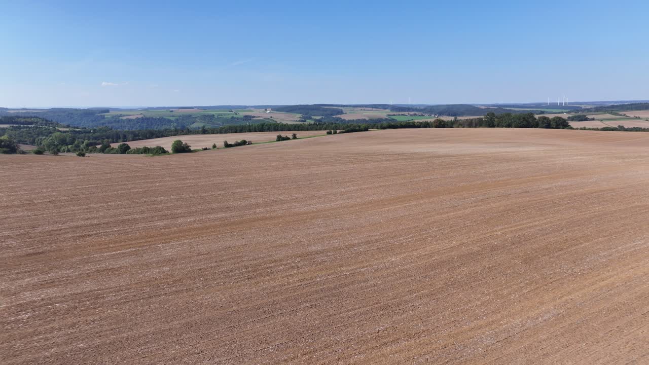 Aerial shot of a dry, harvested field in the summer with a panoramic green landscape in the background