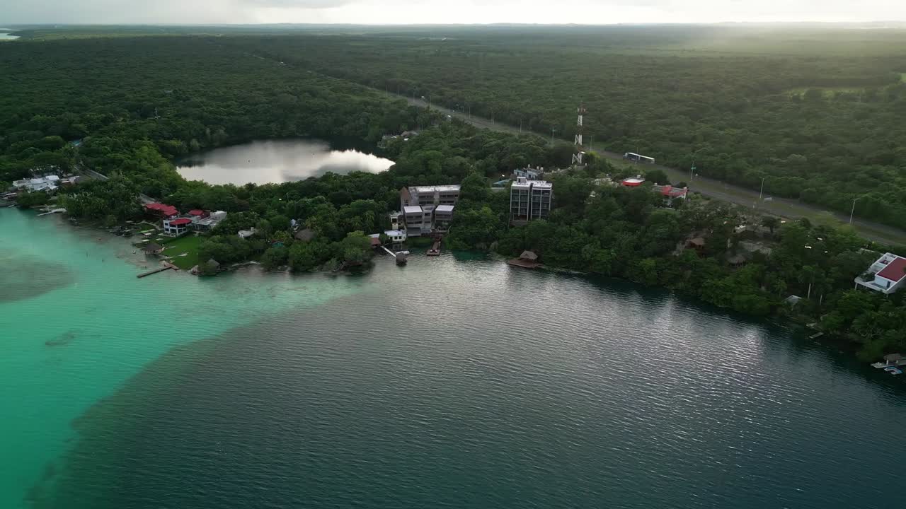 Aerial view over Bacalar, Quintana Roo, Mexico, reveals lush jungle, lakeside resorts, and the large visible cenote near the turquoise waters of the famed lagoon