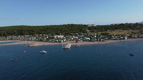 Drone-Acercándose-A-Un-Camping-De-5-Estrellas-En-Croacia-Krk-Desde-La-Costa-Con-Niños-Divirtiéndose-Y-Rv-Campmobiles-En-Un-Brillante-Día-De-Verano