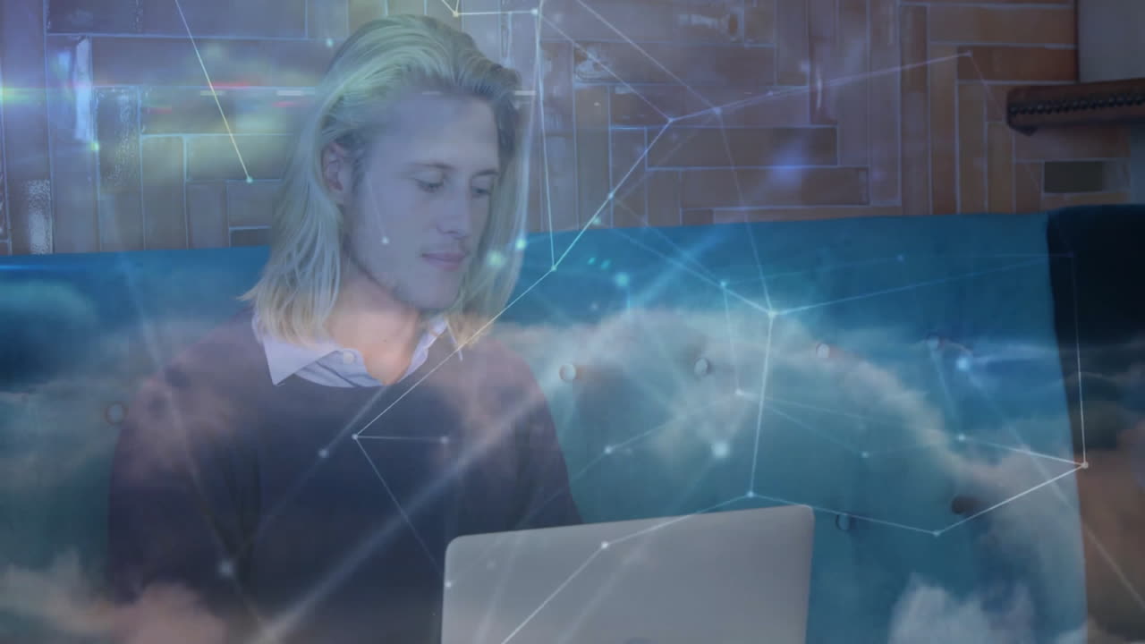 IT pro leaning on teal sofa, interacting with laptop overlaying cloud network graphics