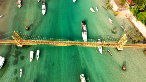 Beliebte-Gelbe-Brücke-In-Indonesien,-Die-Die-Inseln-Nusa-Lembongan-Und-Nusa-Ceningan-Auf-Bali-Verbindet,-Mit-Booten,-Die-Auf-Dem-Türkisfarbenen-Meerwasser-Schwimmen