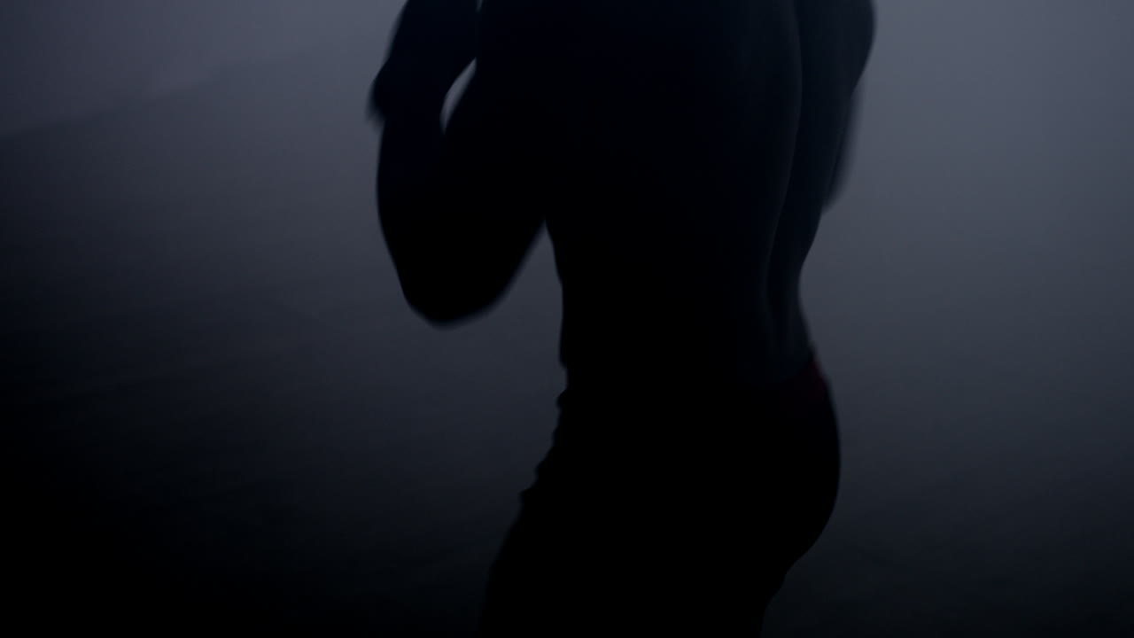 силуэт боксера тренируется на темном ринге. боец пинает воздух. концепция боя