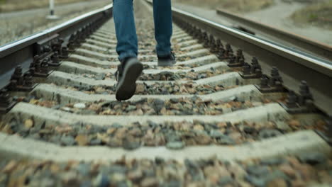 a close view of someone running on a railway track, wearing jeans and canvas shoes, the track is covered with stones with a blur surrounding