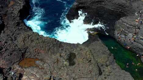 Toma-Aérea-De-Una-Laguna-Rocosa-Y-Una-Piscina-Natural-Con-Nadadores