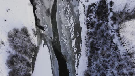 Long-Narrow-Road-Over-Frozen-River-Through-Winter-Forest-Mountains---Aerial-Drone-Shot,-Reveal