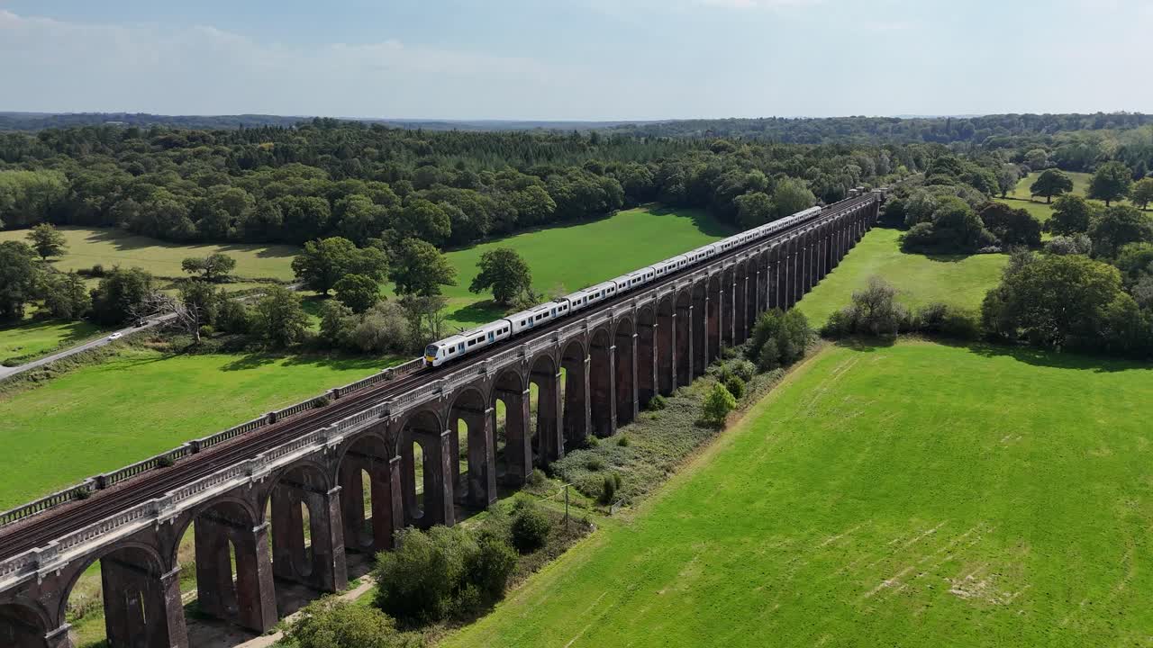 Majestic aerial footage of Ouse Valley Viaduct. Passenger train sweeps across the bridge, highlighting Victorian architecture, arches, and the surrounding South Downs scenery