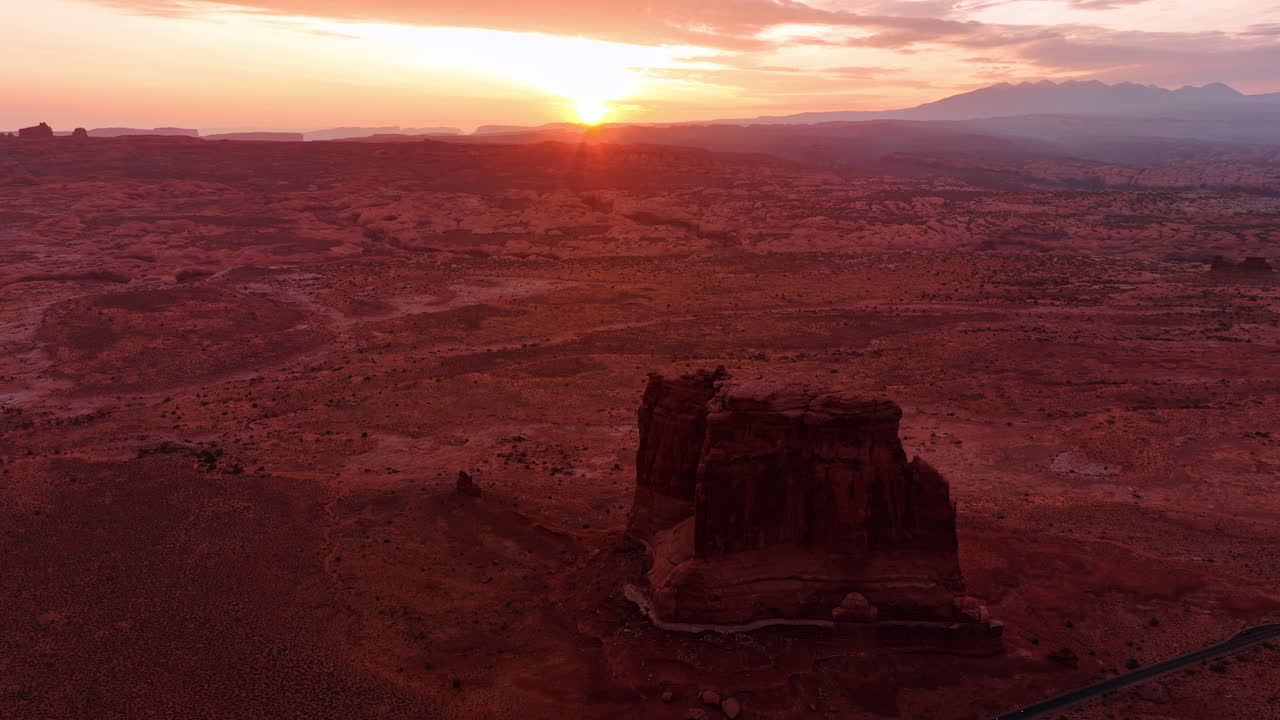 Sun sets over the horizon coloring the scenery in red. Drone footage approaching the rock in the Arches National Park in Utah, USA