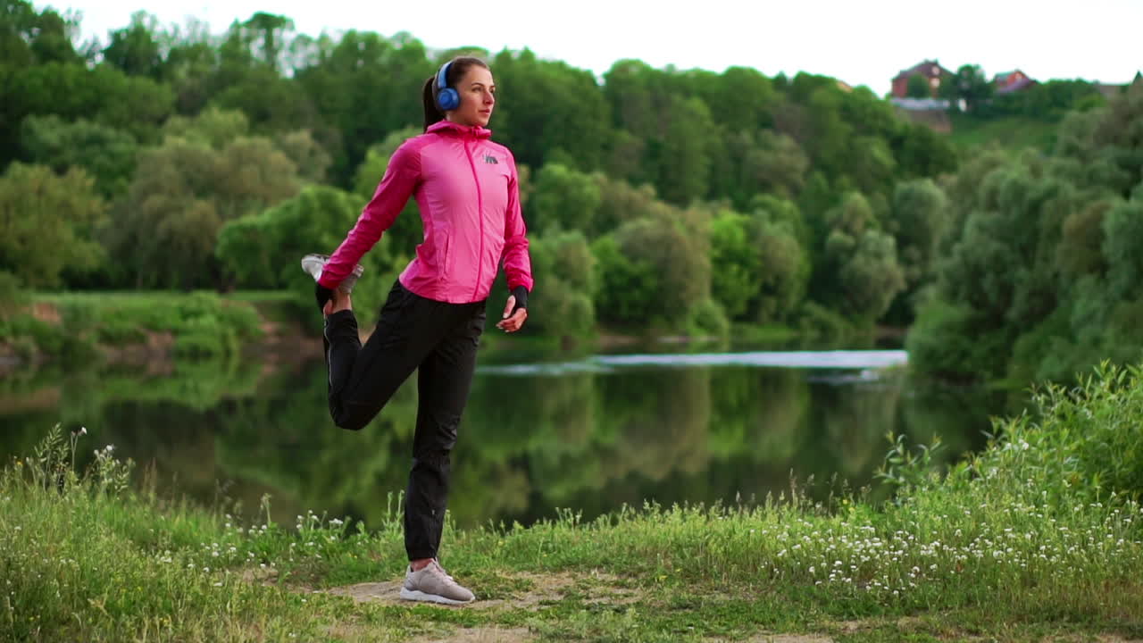 A girl in a pink jacket is preparing for a run warm up and listen to music in headphones through the phone