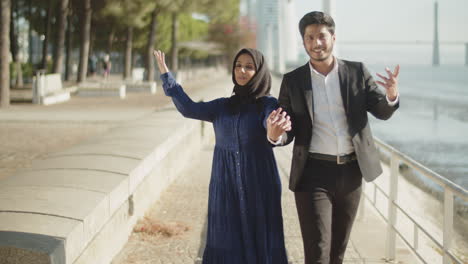 medium shot of happy muslim couple walking along quayside