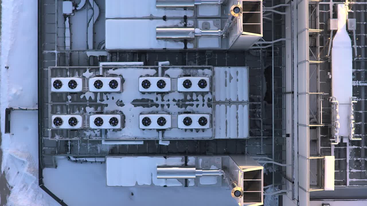 Aerial drone view flying over the roof of a large data center building. Industrial air conditioning and ventilation systems are covered in snow