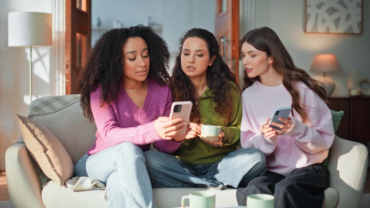 Three friends using smartphones sitting couch home closeup. Group discussing