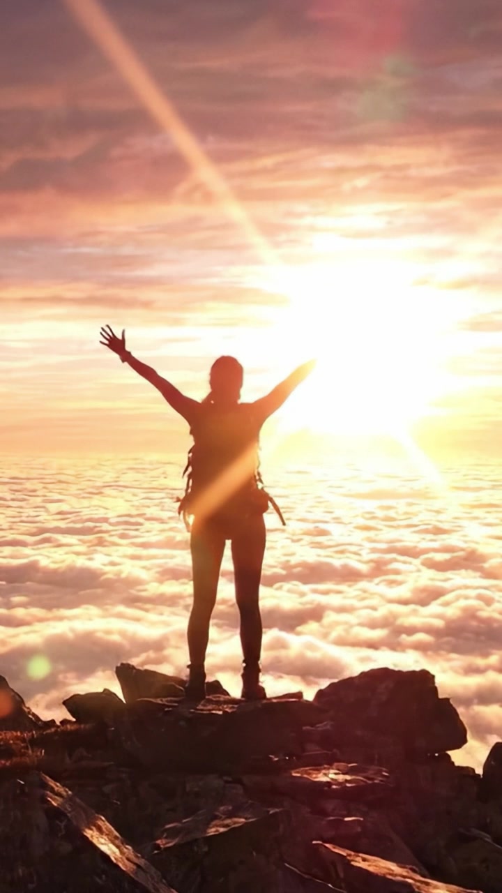 Una sagoma di trionfo: un escursionista raggiunge la vetta all'alba, abbracciando la bellezza delle cime baciate dalle nuvole e i colori vivaci dell'alba.