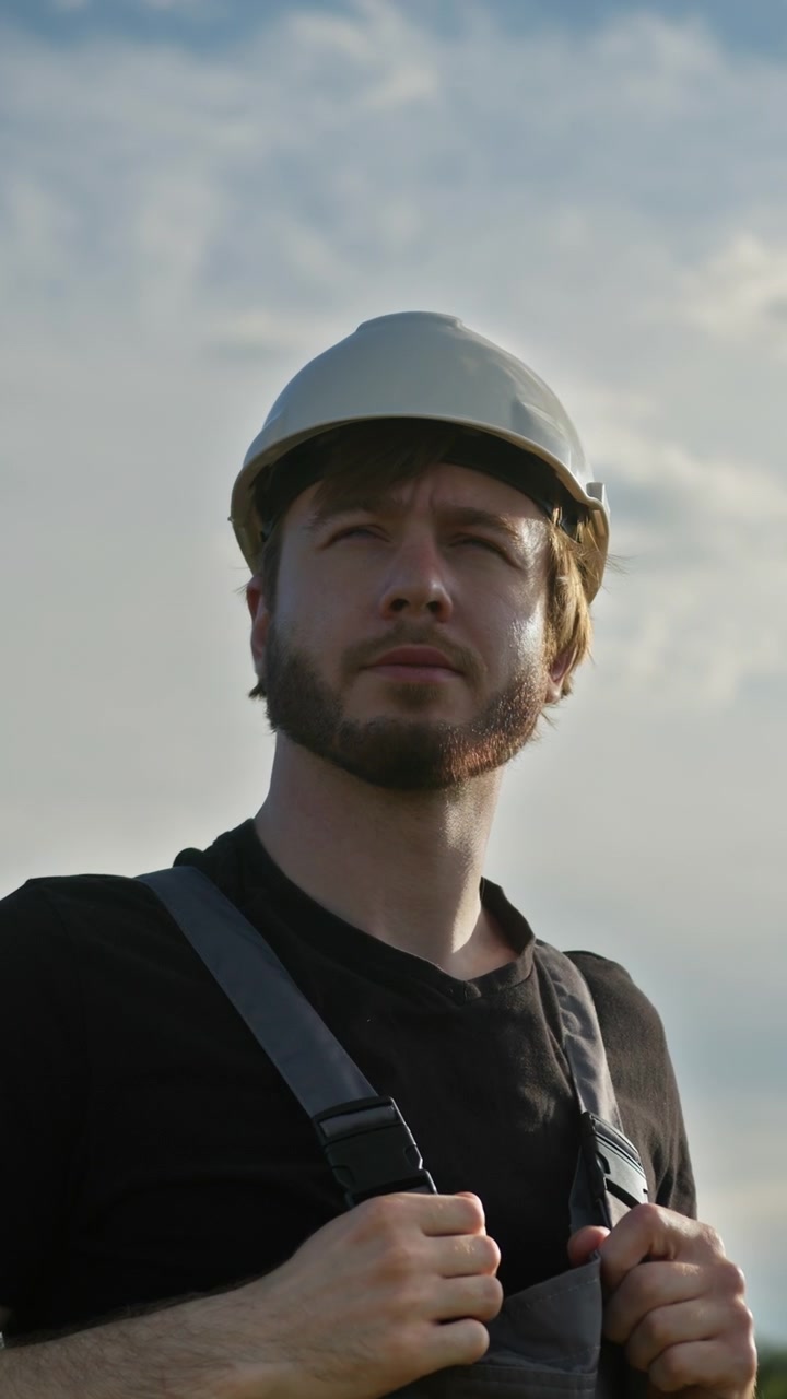 Uomo con cappello e tuta da lavoro guarda pensieroso verso il cielo in una giornata nuvolosa, trasmettendo un.