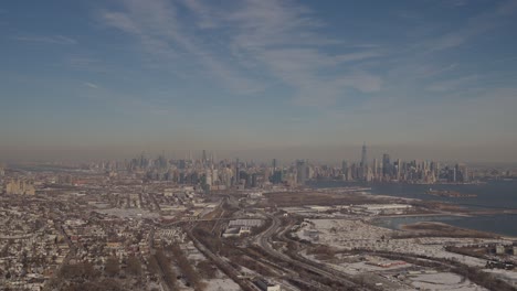 expansive aerial view of manhattan’s skyline with liberty state park, snowy roads, and the urban sprawl of new jersey in the foreground under blue skies.