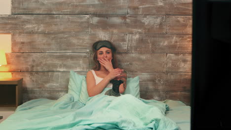 una mujer bonita en pijama asustada de una película de terror en la televisión.